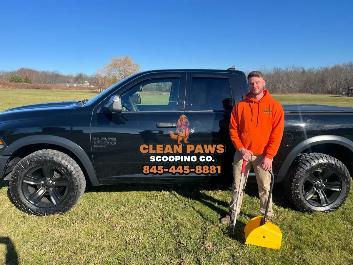Clean Paws technician in an orange hoodie beside the branded service truck holding scooping tools